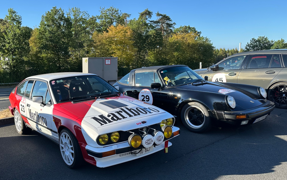 A Marlboro-branded Alfa Romeo Alfetta GTV6 stands beside a black Porsche 911